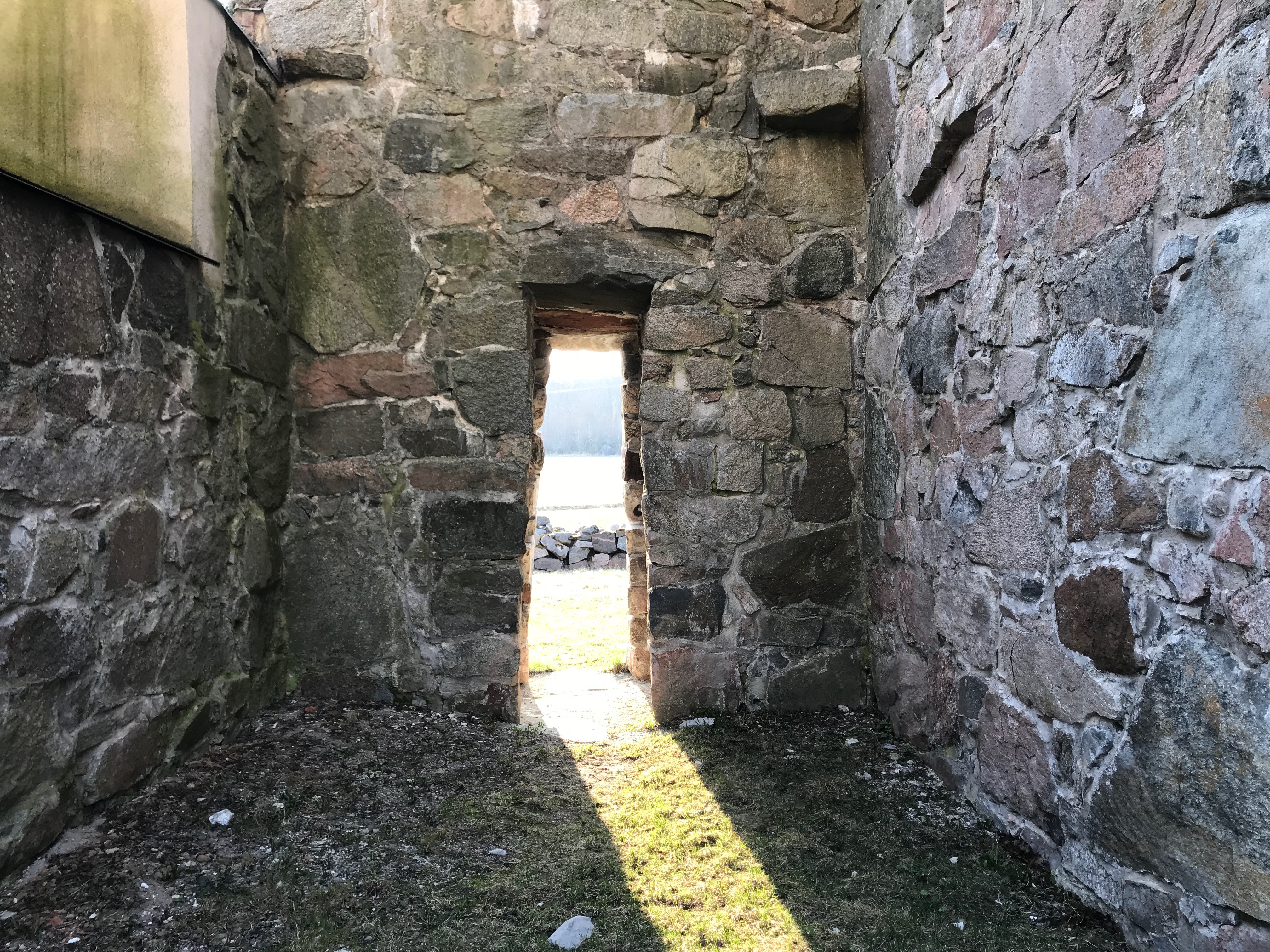 Foto inifrån en ruin, ut genom en smal dörr motett soligt landskap